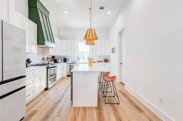 a kitchen with stainless steel appliances granite countertop a sink dishwasher a stove and white cabinets with wooden floor