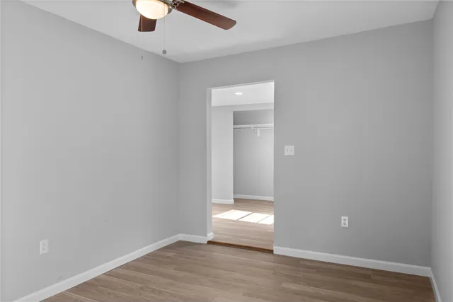 an empty room with wooden floor fan and windows