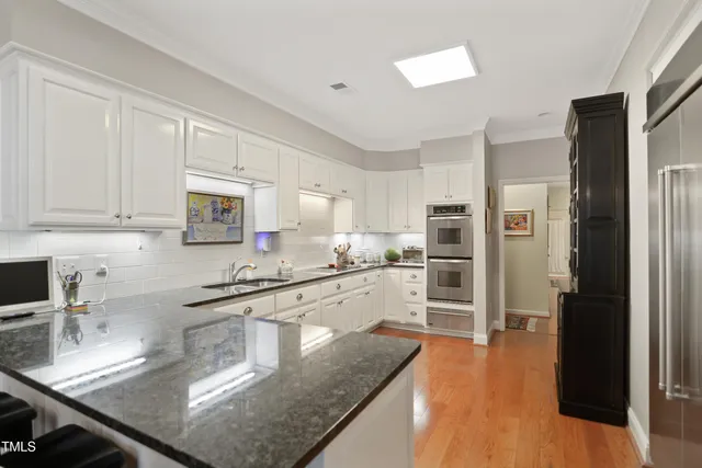 a kitchen with stainless steel appliances granite countertop a refrigerator a sink dishwasher a stove and white countertops with wooden floor