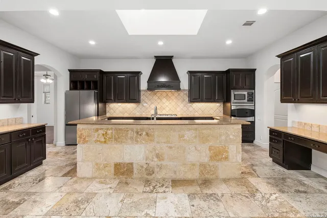 a kitchen with stainless steel appliances granite countertop a stove top oven a sink dishwasher and a refrigerator with wooden floor