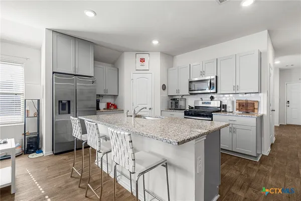 a kitchen with stainless steel appliances granite countertop a table chairs sink and cabinets