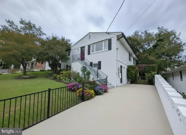 a view of a white house with a small yard plants and a large tree