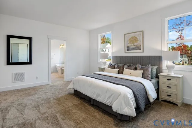 a spacious bedroom with a bed and a lamp on dresser