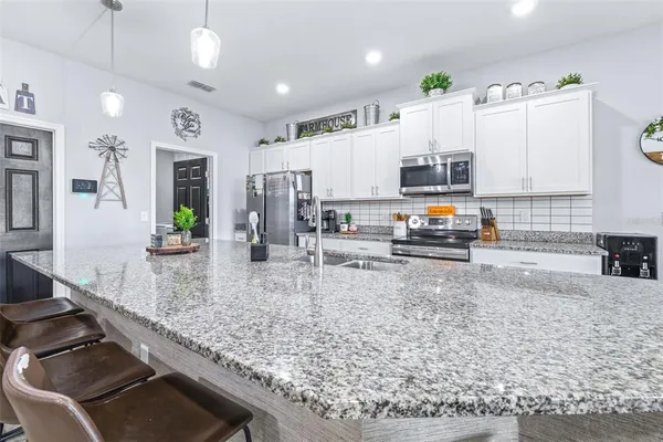 a kitchen with stainless steel appliances granite countertop a refrigerator a oven a sink a dining table and chairs with wooden floor