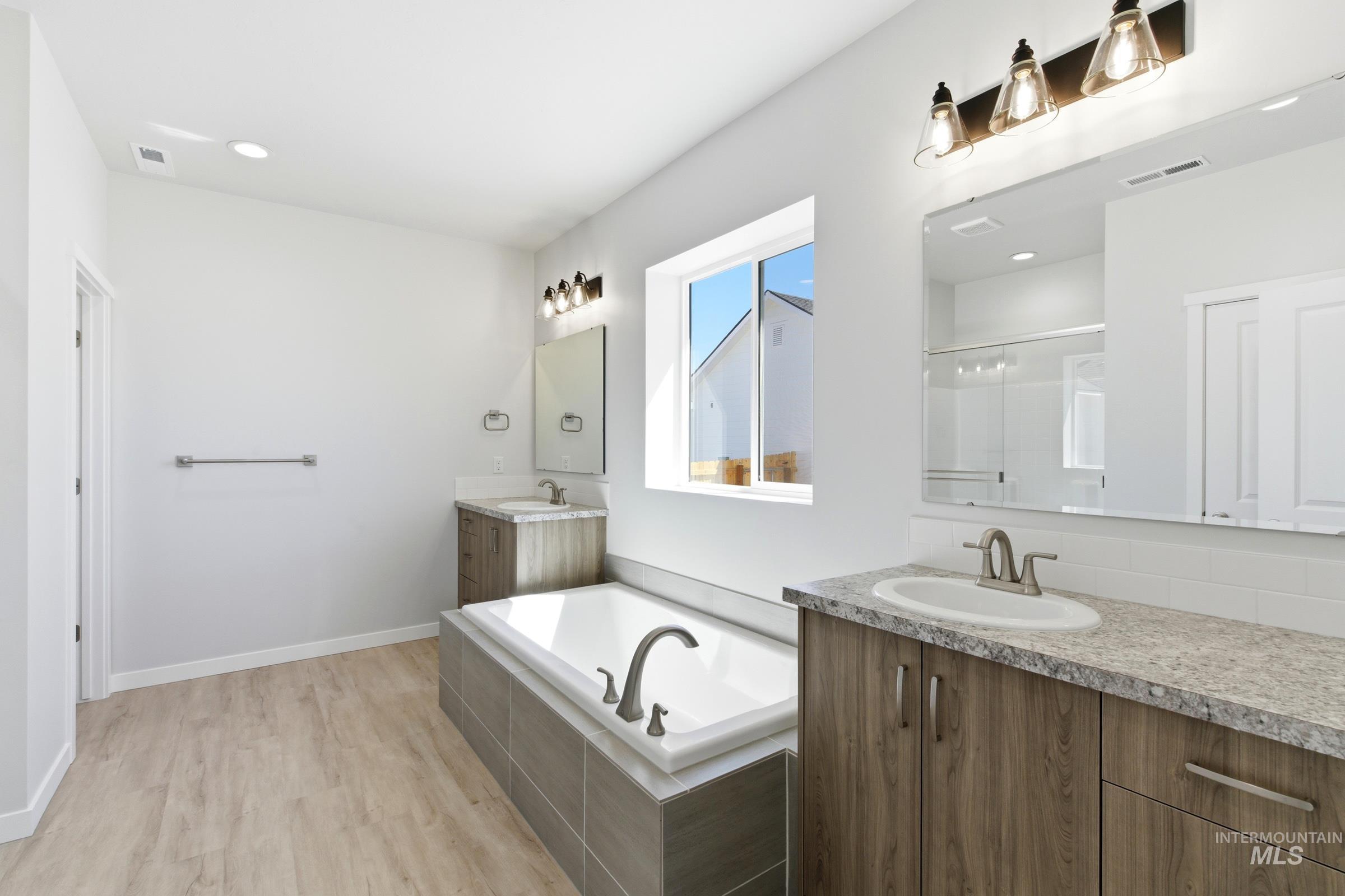 13663 Redway Court Caldwell, ID 83607 - Photo 30 of 32 Spacious bathroom featuring a built-in soaking tub, wood-finish flooring, dual vanity sinks with light-toned countertops, and contemporary lighting fixtures