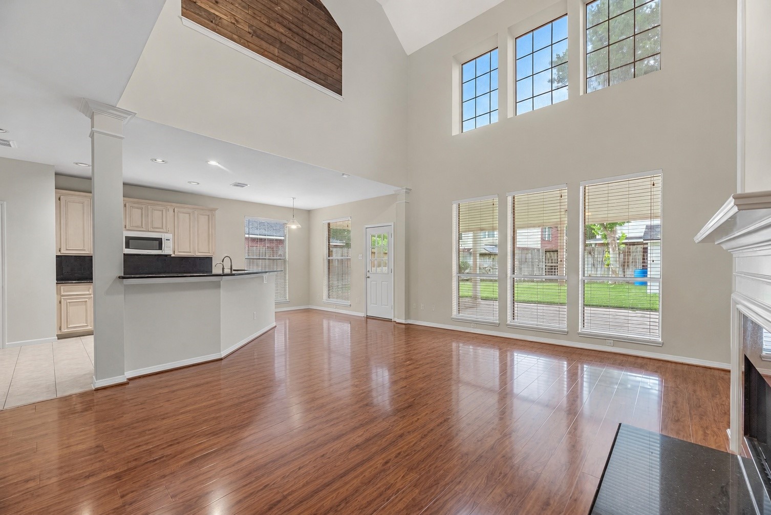 5724 Shady Hollow Court Rosharon, TX 77583 - Photo 25 of 27 Bright open-concept living area showcasing soaring ceilings, expansive windows, glossy wood-look flooring, and a cozy fireplace. The adjacent kitchen features light cabinetry, dark countertops, a breakfast bar, and clear sight lines into the main living space.