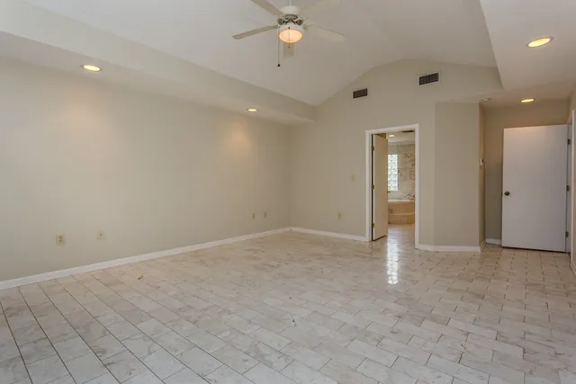an empty room with chandelier fan and kitchen view