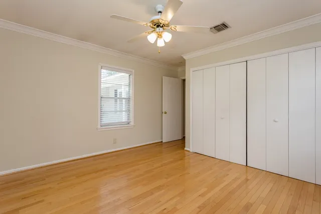 a view of an empty room with chandelier fan and wooden floor