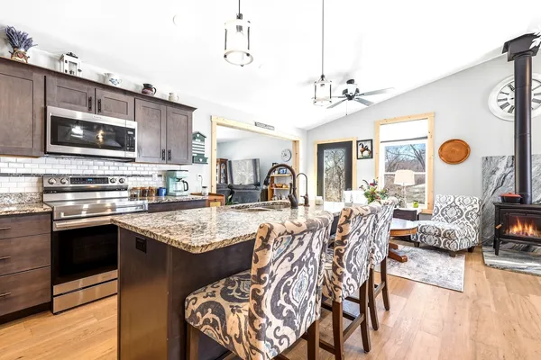 a open kitchen with stainless steel appliances granite countertop a stove top oven a sink dishwasher and white cabinets with wooden floor