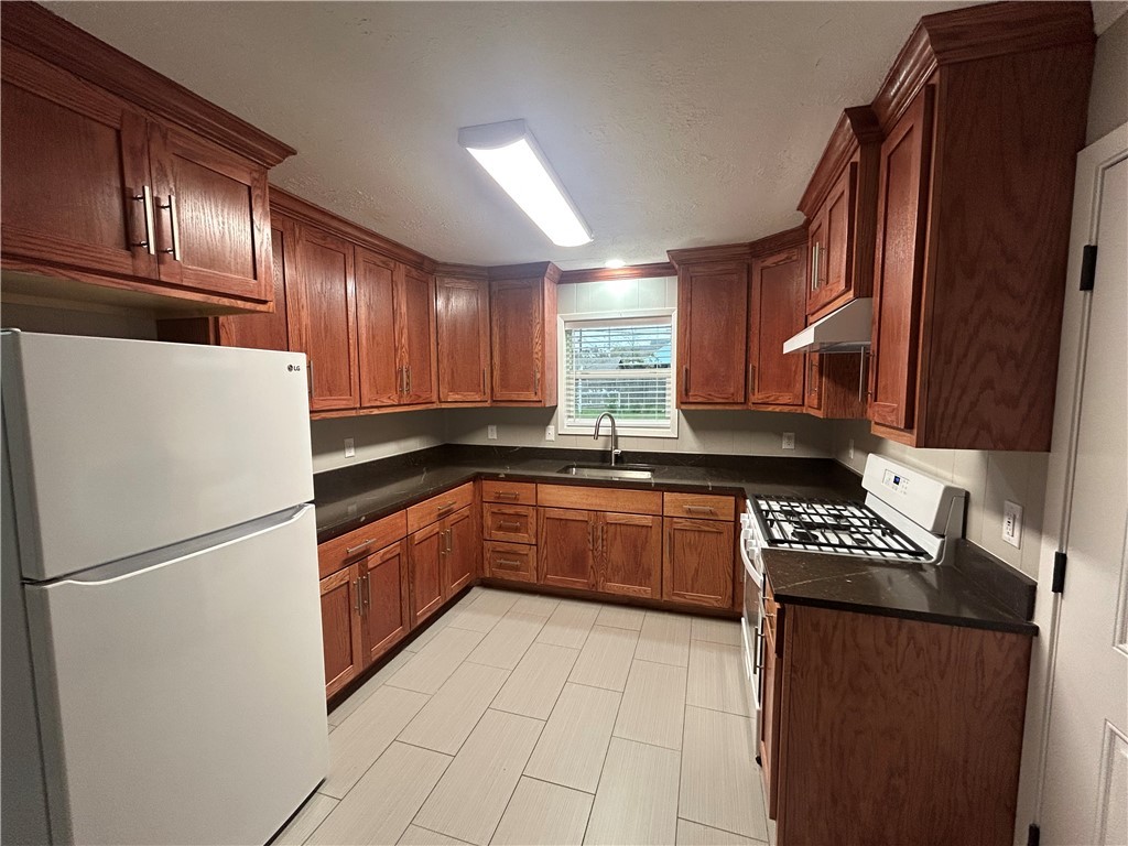 916 South Gordon Street Bryan, TX 77803 - Photo 7 of 8 a kitchen with stainless steel appliances granite countertop a refrigerator a sink dishwasher a stove with wooden cabinets and floors