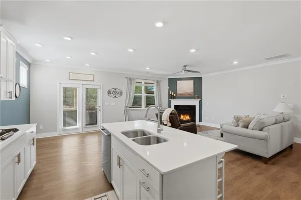 a kitchen with stainless steel appliances kitchen island granite countertop a refrigerator a stove top oven a sink dishwasher and white cabinets with wooden floor