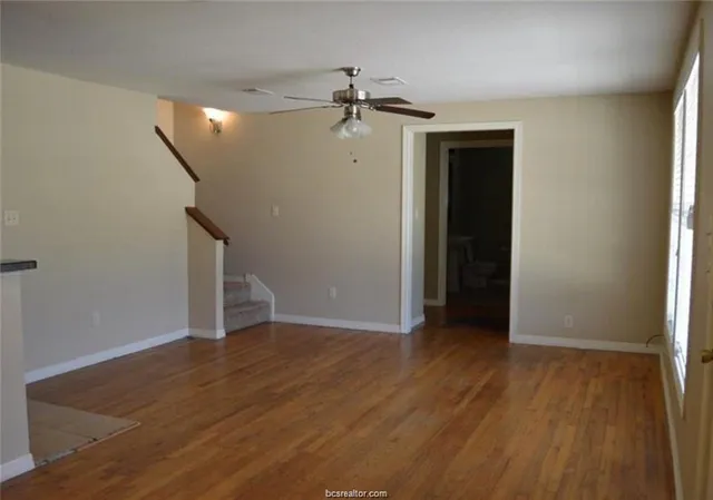 an empty room with wooden floor ceiling fan and windows