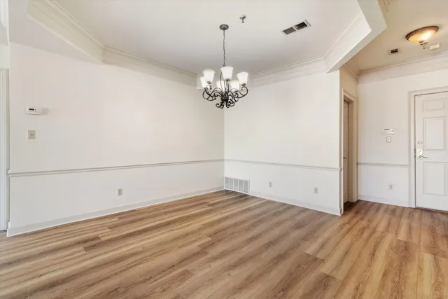 an empty room with wooden floor chandelier and windows