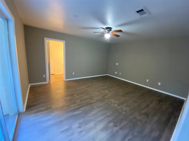 a view of an empty room with wooden floor and fan