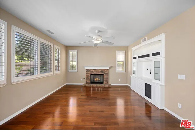 a view of a livingroom with a fireplace a ceiling fan and windows