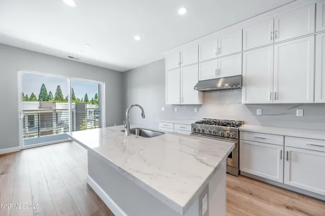 a kitchen with stainless steel appliances granite countertop a stove a sink and white cabinets with wooden floor next to windows