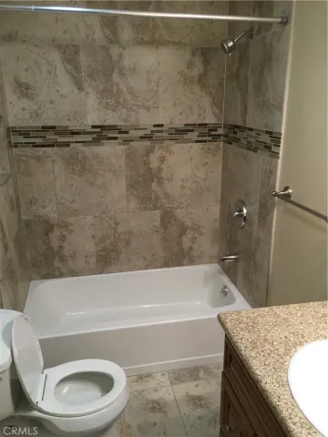 a bathroom with a granite countertop bathtub shower sink vanity and toilet