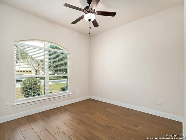 an empty room with wooden floor fan and windows