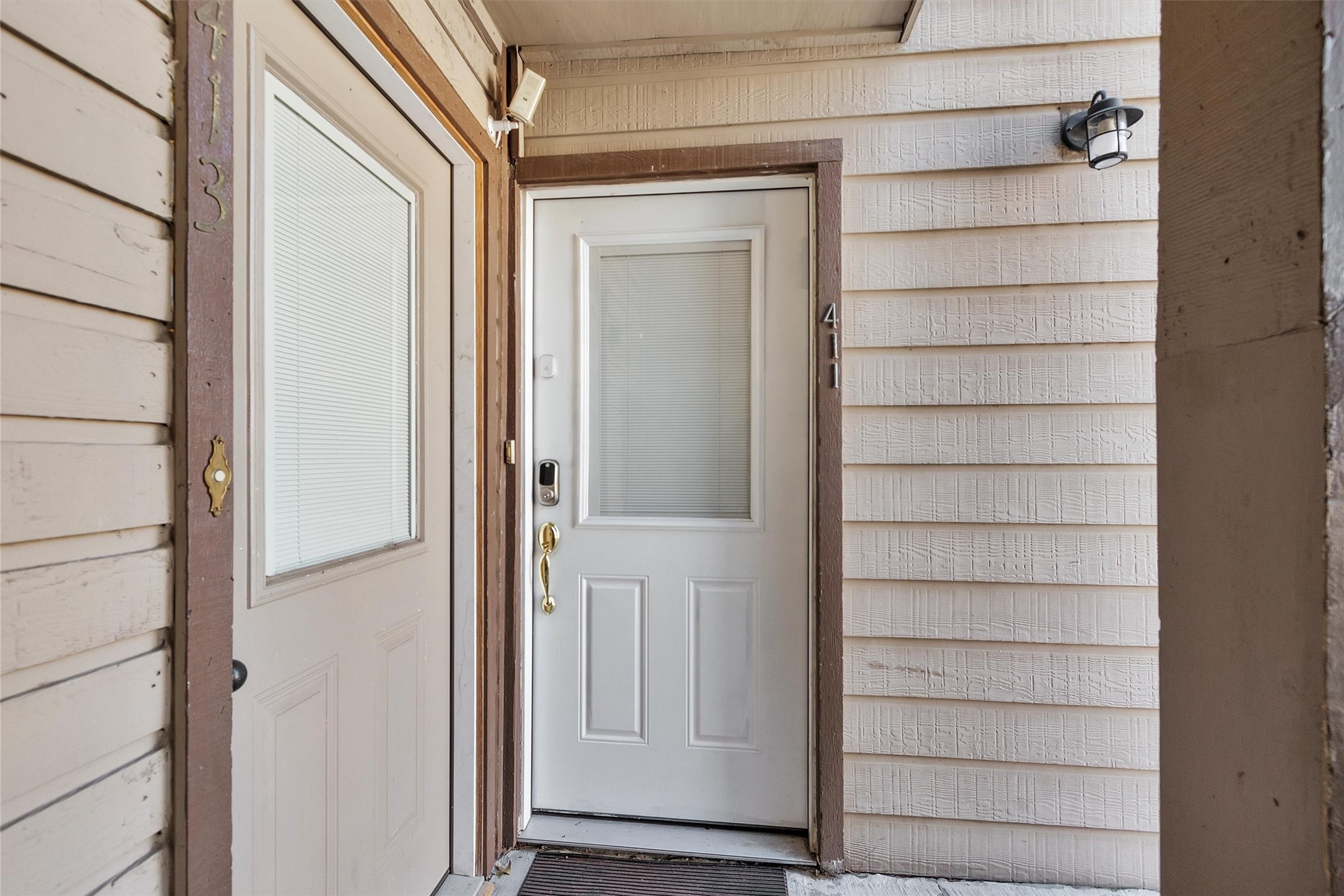 12900 Walden Road, Unit D 411 Montgomery, TX 77356 - Photo 2 of 18 This inviting entryway, with its glass-paneled doors featuring privacy blinds, is warmly illuminated by a wall-mounted lamp and offers a cozy, sheltered ambiance with charming wood siding.