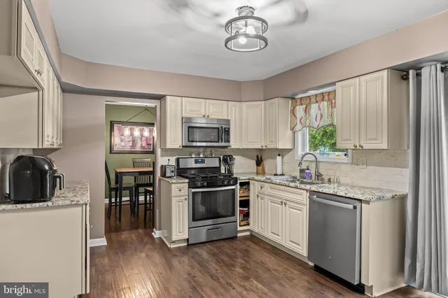 a kitchen with stainless steel appliances granite countertop a stove top oven a sink dishwasher a refrigerator and white cabinets with wooden floor