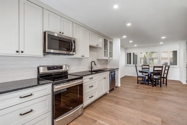 a kitchen with stainless steel appliances kitchen island granite countertop a stove top oven a sink a dining table and chairs with wooden floor