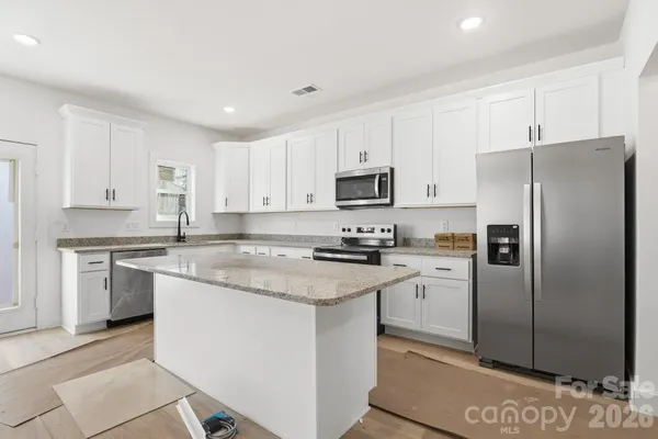 a kitchen with stainless steel appliances granite countertop a refrigerator stove a sink and white cabinets