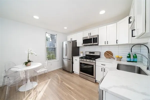 a kitchen with stainless steel appliances a stove a sink a refrigerator white cabinets and wooden floor