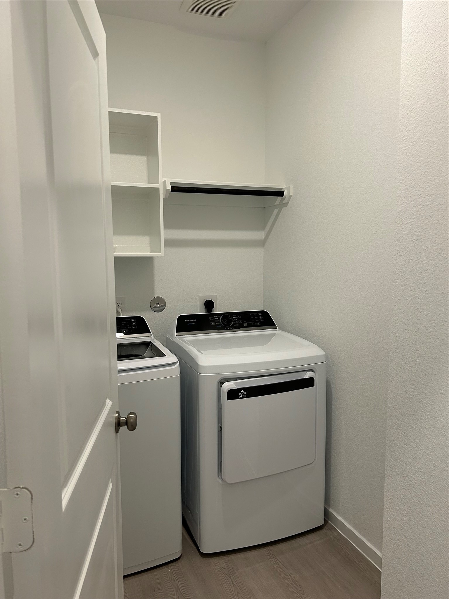 26419 Virginia Wild Rye Lane Katy, TX 77493 - Photo 16 of 31 This photo shows a compact laundry room with a washer and dryer, a shelf, and storage space. The room has light-colored walls and flooring, creating a clean and bright atmosphere.