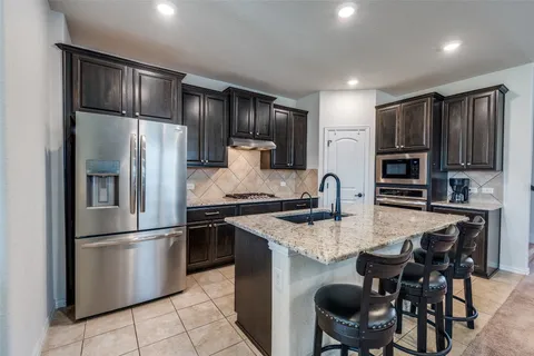 a kitchen with kitchen island granite countertop stainless steel appliances cabinets a sink and a refrigerator