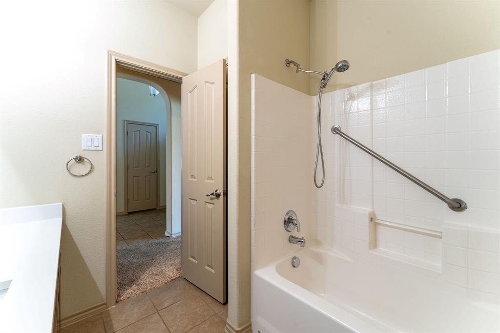 11156 Hawks Landing Road Fort Worth, TX 76052 - Photo 11 of 30 Bathroom featuring a white subway tile pattern, a built-in tub with grab bar, a chrome shower head with handheld sprayer, and a solid quartz surface countertop
