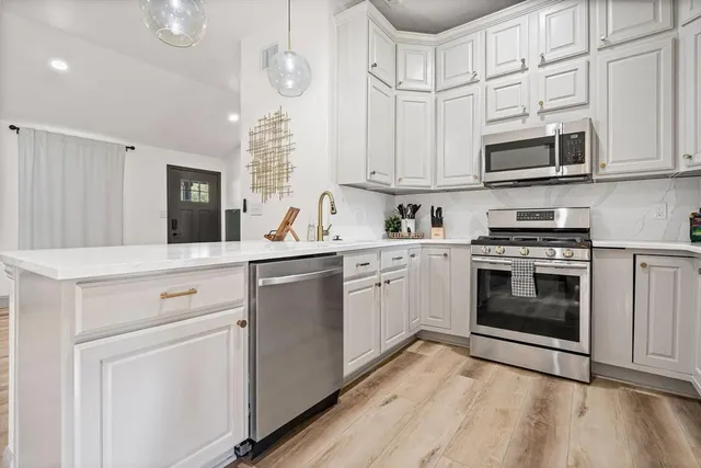 a kitchen with stainless steel appliances granite countertop white cabinets a sink a stove a dining table and chairs