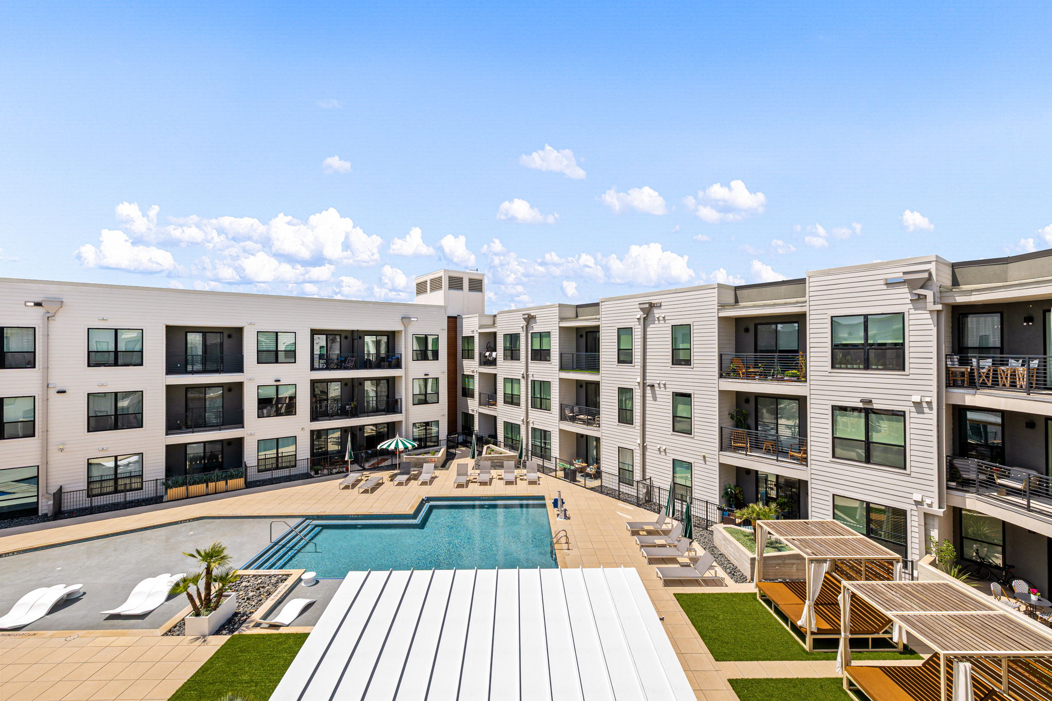 1701 Simond Avenue, Unit 612 Austin, TX 78723 - Photo 25 of 40 Modern multi-story building exterior with balconies, a central swimming pool, integrated lounge areas with cabanas, and artificial turf landscaping