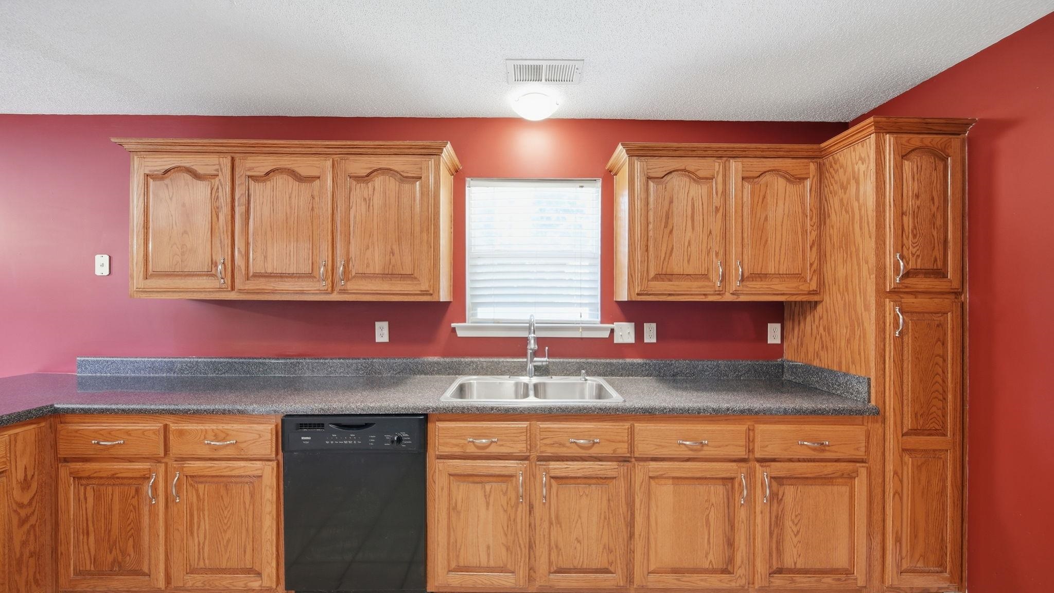 217 Rae Drive Munford, TN 38058 - Photo 17 of 40 Kitchen featuring wood-finish cabinetry, dark speckled countertops, a double basin stainless steel sink, and a built-in black dishwasher
