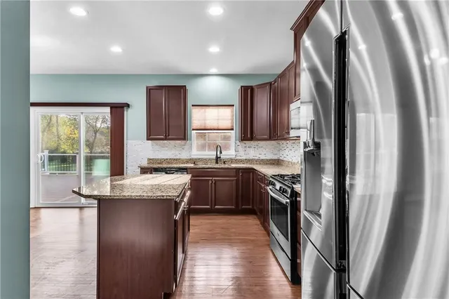 a kitchen with stainless steel appliances granite countertop a refrigerator a sink dishwasher a stove and white cabinets with wooden floor