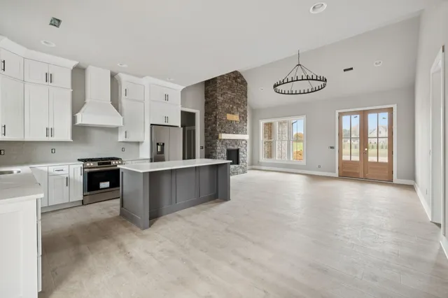 a large kitchen with stainless steel appliances granite countertop a stove a sink dishwasher a refrigerator white cabinets and wooden floor