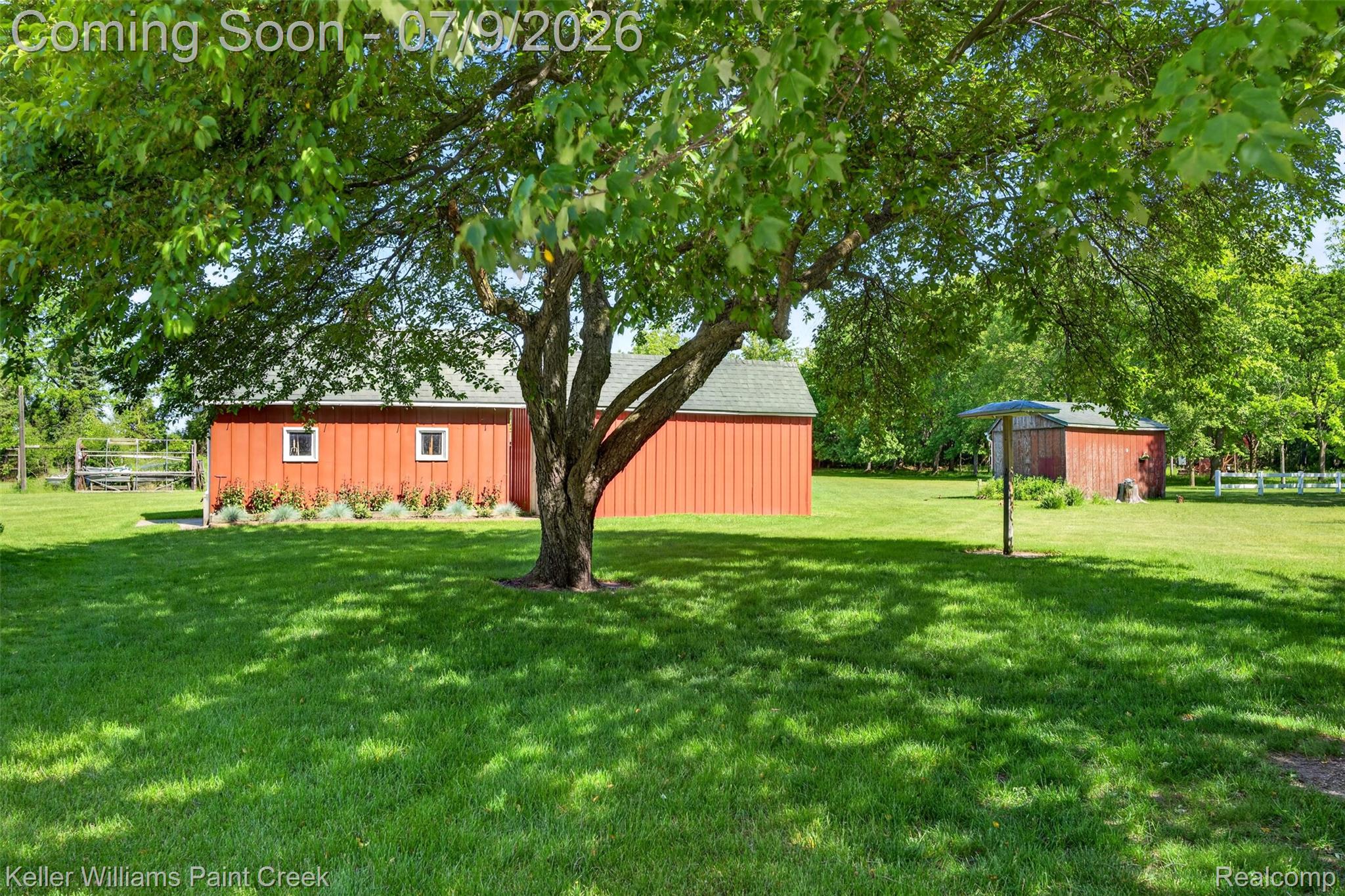 204 Russell Road Kawkawlin, MI 48631 - Photo 7 of 82 Expansive green lawn with mature shade trees, complemented by two red-sided outbuildings featuring white trim and gray roofs