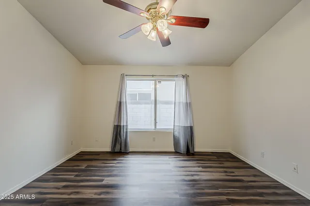 an empty room with wooden floor chandelier fan and windows