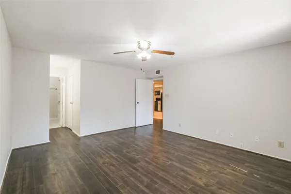 a view of an empty room with wooden floor and a ceiling fan