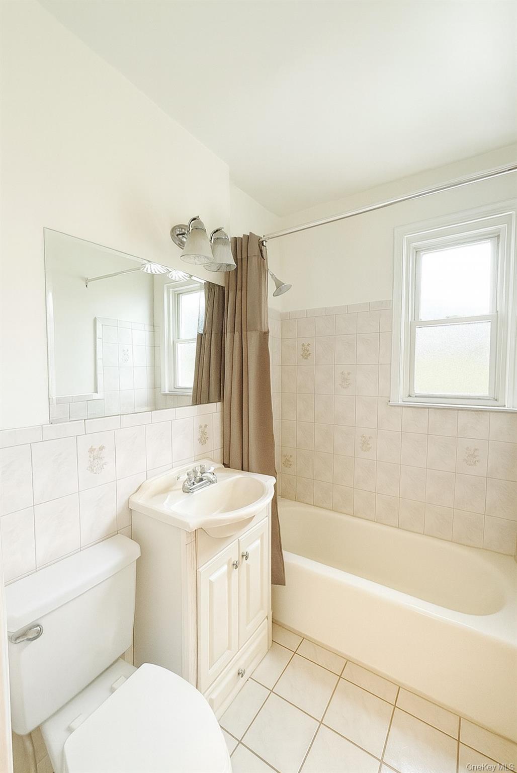 7103 252nd Street, Unit 199B Queens, NY 11426 - Photo 8 of 11 Full bathroom featuring vanity, tile walls, light tile patterned floors, and shower / bath combination with curtain