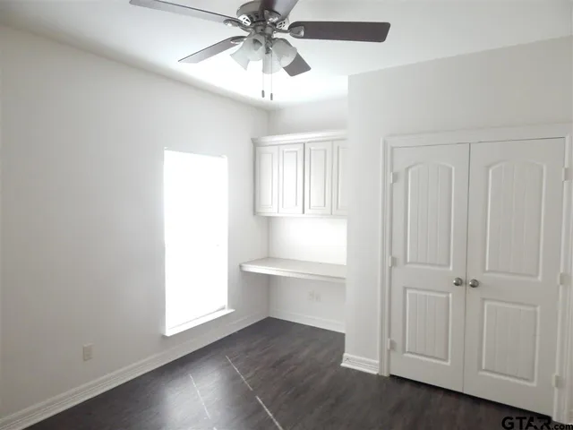 an empty room with wooden floor closet fan and windows