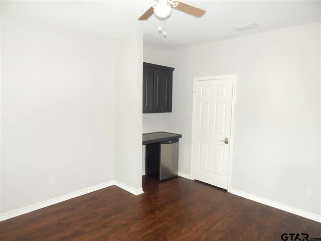 a view of an empty room with wooden floor and a ceiling fan
