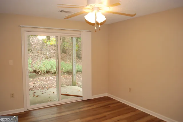 a view of an empty room with wooden floor and fan