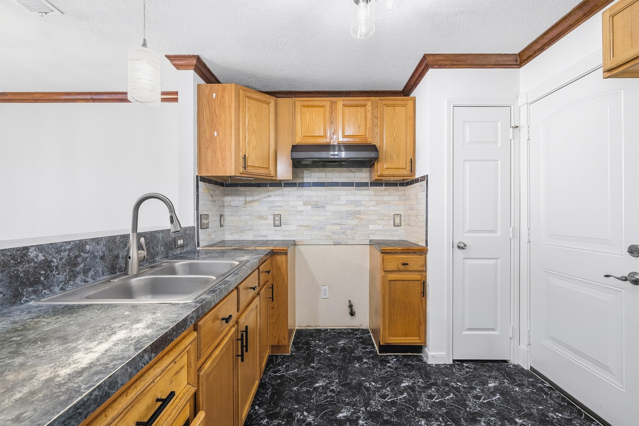5426 Bourgeois Road Houston, TX 77066 - Photo 16 of 43 Charming kitchen with warm wooden cabinetry, sleek black countertops, and a stylish tile backsplash complemented by modern lighting.