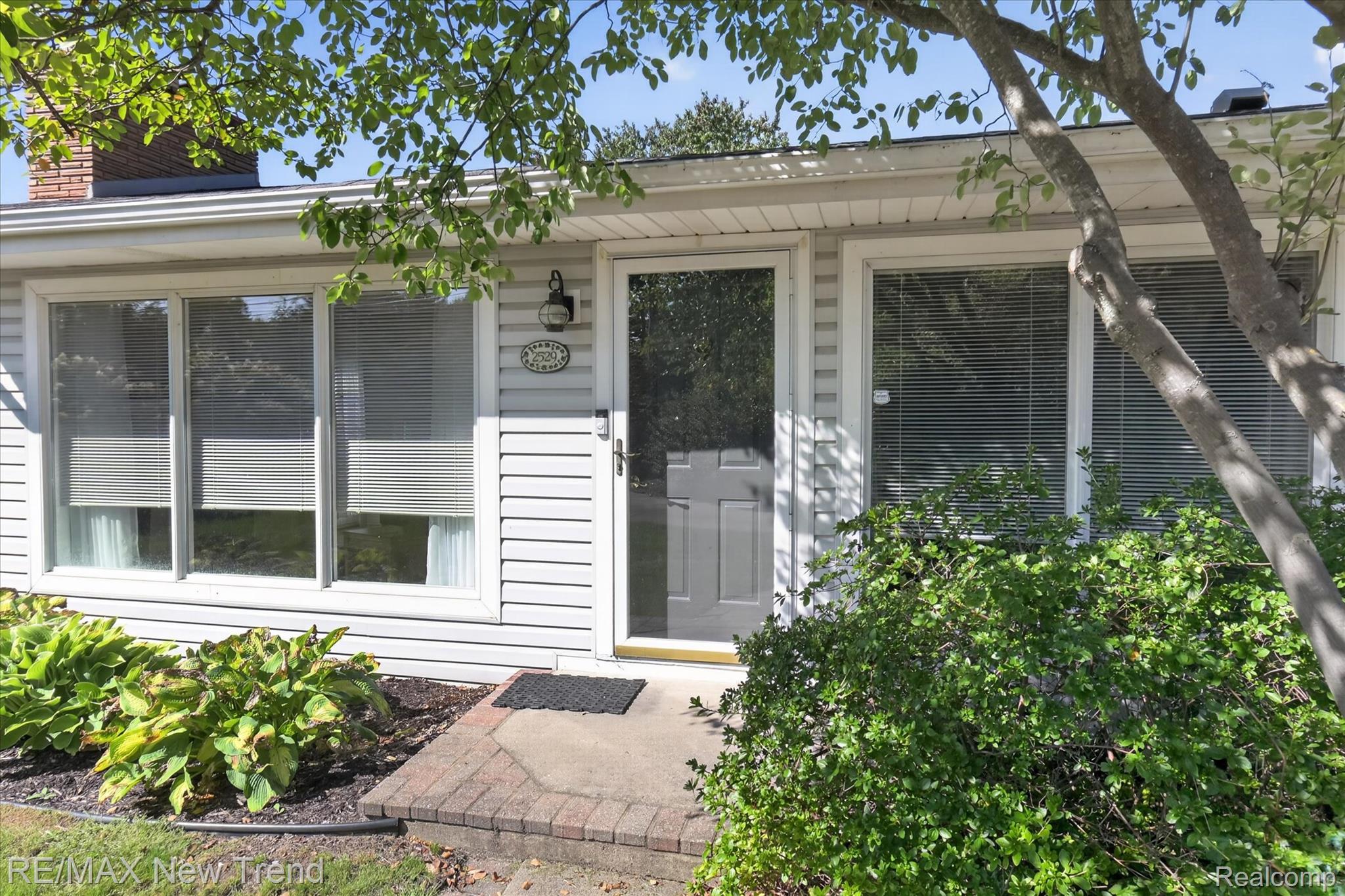 2529 South Commerce Road Walled Lake, MI 48390 - Photo 10 of 66 White horizontal siding, a gray entry door, and multiple windows with blinds, complemented by brick trim and mature landscaping