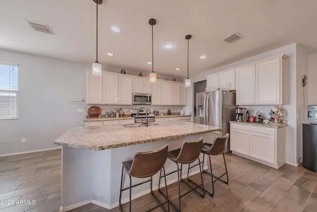 a kitchen with stainless steel appliances granite countertop a sink a stove a refrigerator and white cabinets with wooden floor