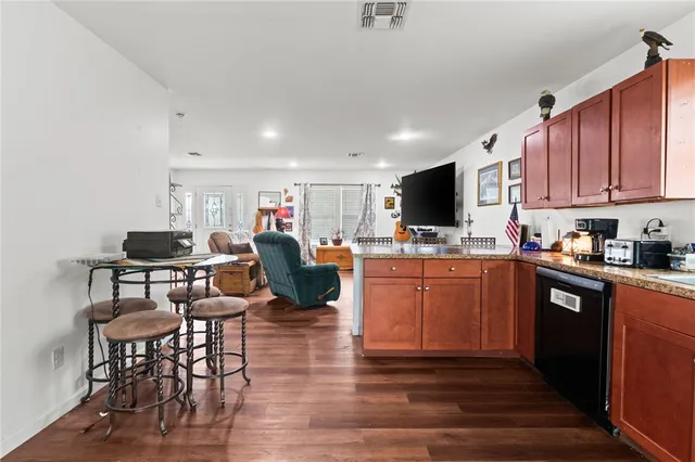 a kitchen with stainless steel appliances granite countertop a stove top oven a sink dishwasher and a dining table with wooden floor