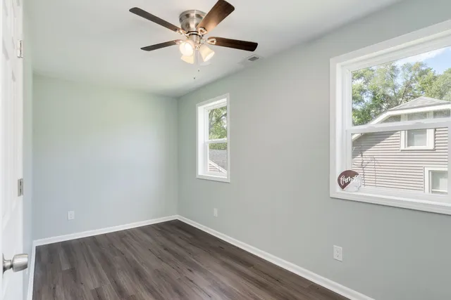 an empty room with wooden floor fan and windows