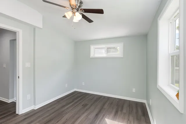 an empty room with wooden floor fan and windows