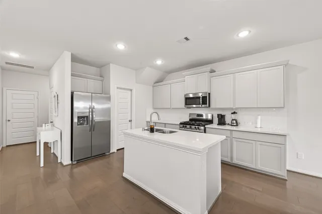 a large kitchen with stainless steel appliances a large counter top a stove a sink a refrigerator and white cabinets