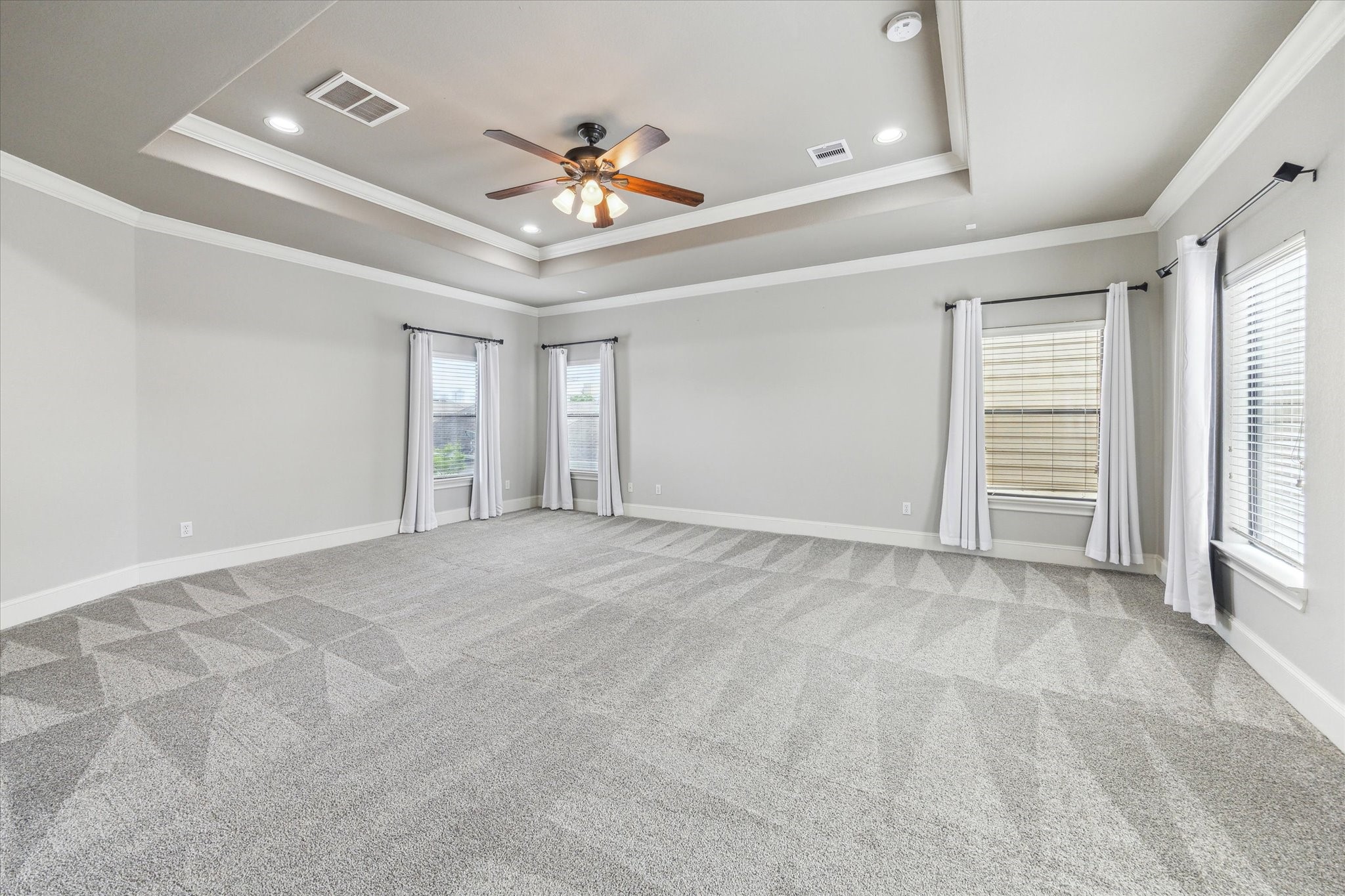 1512 Thompson Street, Unit 3 Houston, TX 77007 - Photo 16 of 32 Spacious, light-filled primary bedroom with plush carpeting, neutral walls, and a tray ceiling featuring a central fan. Natural light streams through multiple windows adorned with white curtains, creating an inviting atmosphere.